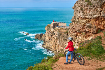 nice senior woman riding her electric mountain bike on the rocky cliffs of Nazare at the western...