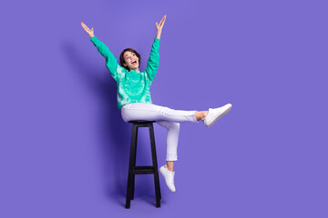 Full size photo of attractive young woman sit chair playful have fun dressed stylish green clothes isolated on violet color background