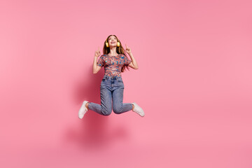 Full length photo of lovely teen jump headphones point look up empty space dressed stylish print clothes isolated on pink color background