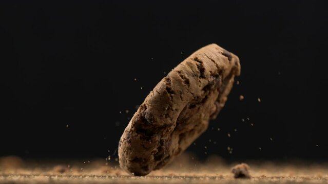 One chocolate chip falls into table surface with crumbs flying in the air captured in super slow-motion at 1000 fps in macro close-up, sugar snack detail