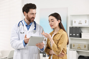 Doctor with tablet consulting patient during appointment in clinic