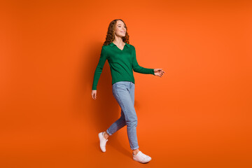 Full length photo of funky cheerful lady dressed green shirt walking empty space isolated orange color background