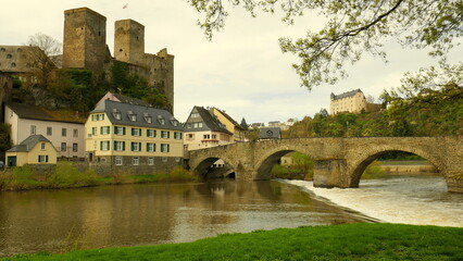 Obraz premium alte Burg Runkel über der Lahn mit Wasserfall und alter Bogenbrücke unter sonnigem Himmel