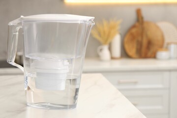 Water filter jug on white marble table in kitchen, space for text