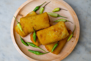 Risoles, a snack from Indonesia served with a little green chili in a wooden plate. Risol and green chilies isolated on a white background