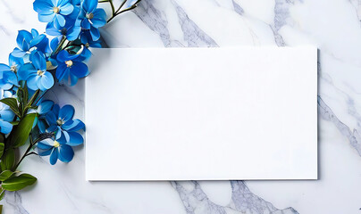 Beautiful work decorated with a blank page and blue flowers on a white marble top view. Copy-space, place for your lettering. 