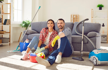 Portrait of happy smiling couple man and woman sitting in the living room at home with vacuum...
