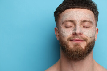 Handsome man with facial mask on his face against light blue background, space for text
