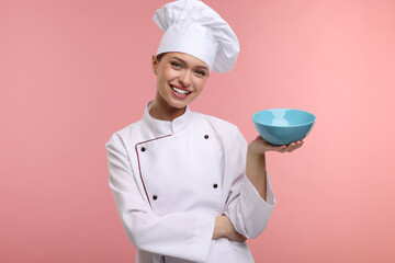 Happy chef in uniform holding bowl on pink background