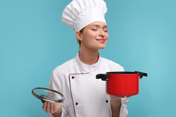 Happy woman chef in uniform holding cooking pot on light blue background