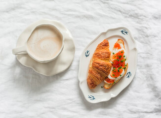 Delicious breakfast, brunch, snack - cappuccino and croissant cottage cheese, egg, red caviar sandwich on a light background, top view
