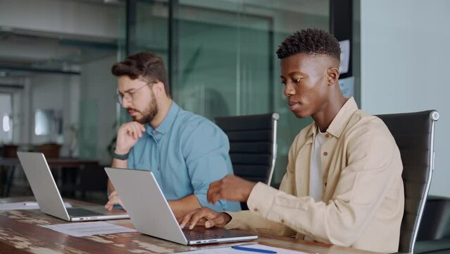 Professional young businessmen colleagues workers typing on computer technology at office workplace desk. Two busy diverse business men company employees using laptops working in office.