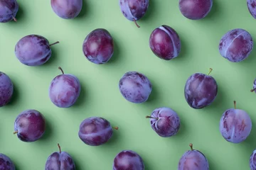 Schilderijen op glas Ripe plums on a vibrant green background in a flat lay composition from above © SHOTPRIME STUDIO