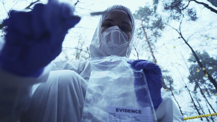 Woman forensic expert works at a crime scene, collecting evidence in a plastic bag, focusing on the...