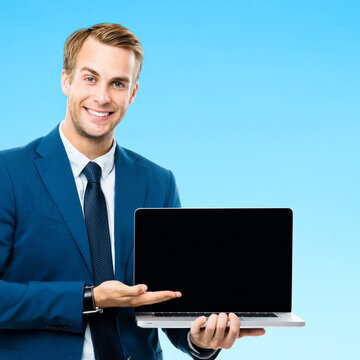 Smiling businessman wear suit, showing laptop with empty black screen monitor, isolated blue marine background. Young happy man at studio concept. Copy space. Square image