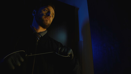 Cruel criminal prepares to attack a victim, lurking in a dark room, at a crime scene during a murder attempt 