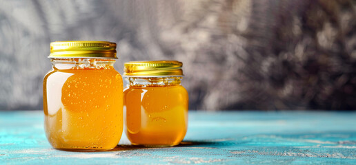 Two jars of fresh honey with golden lids on turquoise surface, sparkling bubbles visible. Frosted background highlighting jars