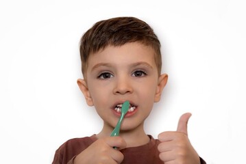 A shot of a little boy with dark hair brushing his teeth against a white background. Health, the topic of healthy teeth in children, hygiene.