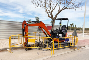 Mini Excavator at constrruction site on road work. Mini excavator digg trench to lay cables concrete curbs and paving slabs at construction site. Backhoe on roadworks and road maintenance.