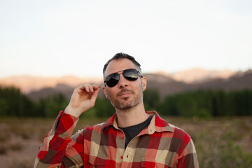Portrait of a man wearing a red flannel and sunglasses, in the desert at sunset. 