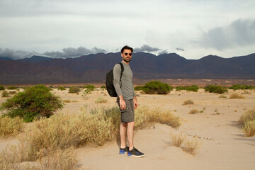 Portrait of a caucasian man wearing sunglasses and a bag, hiking in the desert. The mountains in the background. 