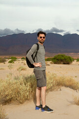 Portrait of a caucasian man wearing sunglasses and a bag, hiking in the desert. The mountains in the background. 