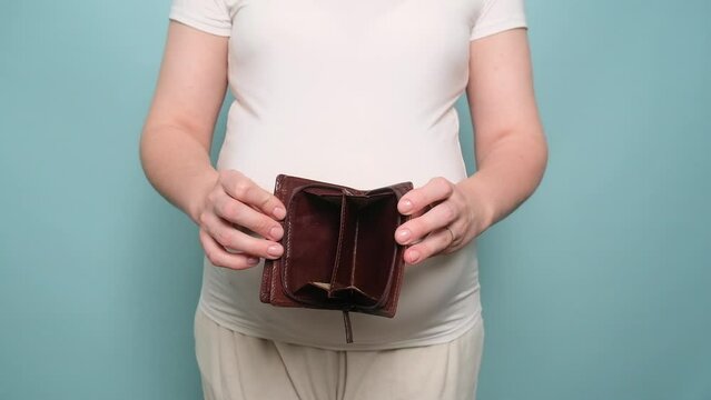 Pregnant woman holding an empty wallet without money in her hand, studio blue background