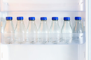 Row of cold water bottles on a shelf in refrigerator with warm light on, good background for refreshing or healthy drinks concept.