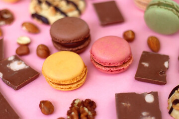 Pastel macarons, almond chocolate, peanut butter cookies and various nuts on bright pink background. Selective focus.