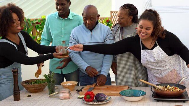 Happy african family cooking together healthy food at house terrace druing summer time - Black parents and adult children having fun outdoor 