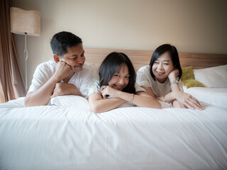 Parents and daughter reclined comfortably on a soft bed. in the hotel. Family vacation on vacation - obrazy, fototapety, plakaty