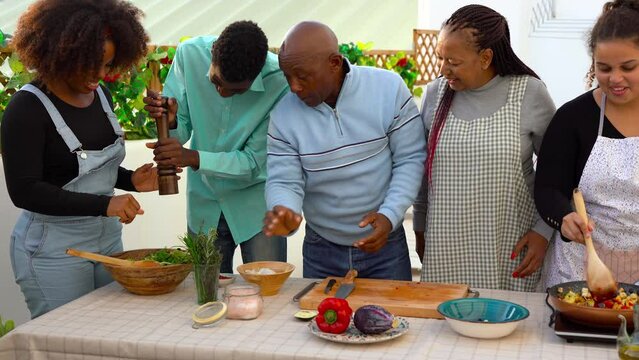 Happy african family having fun cooking together healthy food at house terrace druing summer time	