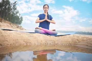 Foto op Plexiglas sukhasana, young indian women sitting in a lotus position doing prayer pose yoga in the sand beach with a reflection on water © Dharma