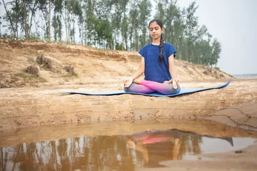 Foto op Plexiglas yoga women practicing padmasana or lotus position yoga in the sand beach showing gyana mudra with a reflection on water © Dharma