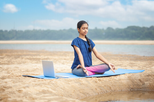zen-like, modern indian women sitting in a padmasana or lotus position doing sukhasana yoga with gyana mudra hand yoga using laptop