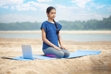 young fitness women doing vajrasana yoga in the tranquility beach using laptop