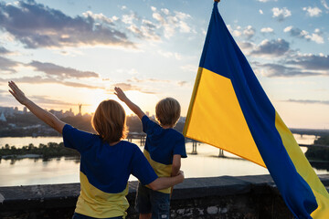 Mom and son with the Ukrainian flag stand high on the roof against the background of the sky and...