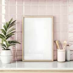 Wall art mockup of vertical blank frame on countertop beside potted plant. Blush pink tiles wall in kitchen interior.