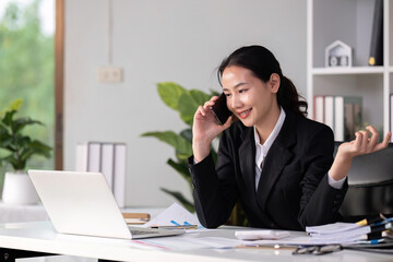 Asian female accountant Discussing business over the phone in an office with work plan documents on the table