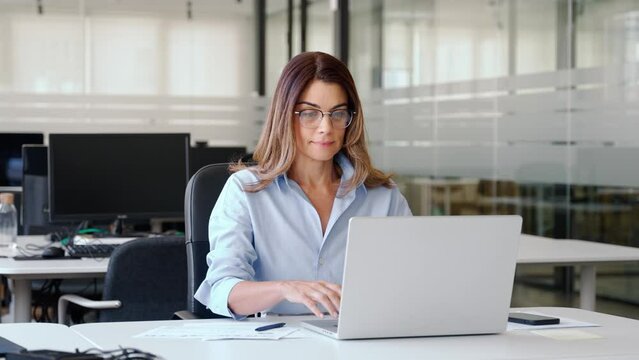 Happy busy mature business woman entrepreneur in office using laptop at work, smiling professional middle aged female company executive manager working looking at computer at workplace.