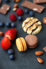 Macarons, chocolate, cookies, berries and various nuts on dark blue background. Selective focus.
