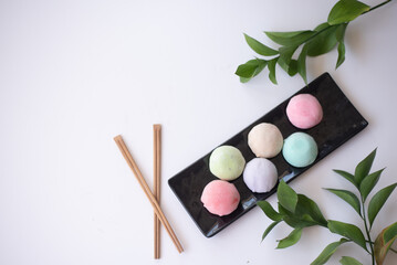 Six mochi different tastes and colors on black plate with green leaves on white background. Japanese traditional frozen delicious dessert mochi. ice cream with dough of sticky rice. asian cuisine