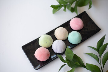 Six mochi different tastes and colors on black plate with green leaves on white background. Japanese traditional frozen delicious dessert mochi. ice cream with dough of sticky rice. asian cuisine