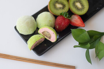 Cut mochi light green color on black plate with kiwi and strawberry on white background. Japanese...