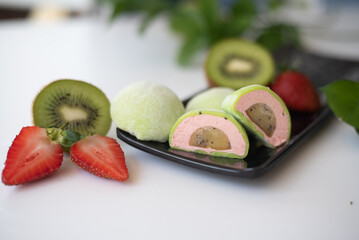 Cut mochi light green color on black plate with kiwi and strawberry on white background. Japanese traditional frozen delicious dessert mochi. ice cream with dough of sticky rice. Asian cuisine.