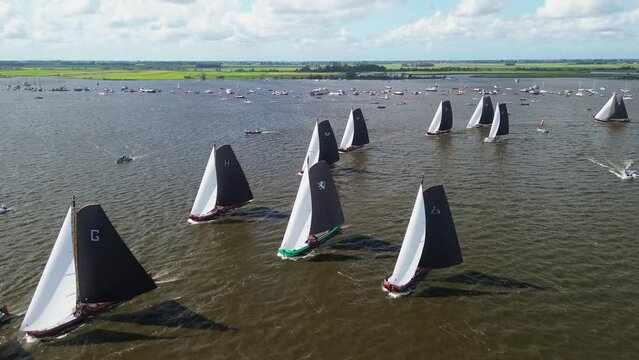 Aerial drone view of traditional Dutch wooden flat bottomed sailboats, skutsje, sailing a race on a Friesian lake in summer. Historic skutsjesilen, national heritage for Holland