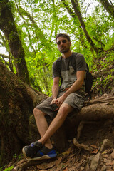 View of a caucasian man wearing sunglasses sitting on a tree trunk in the forest. 