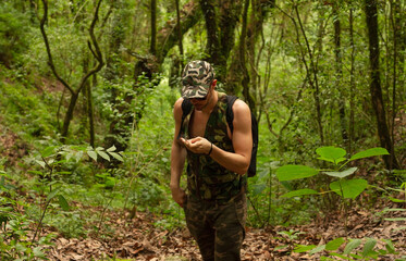 Guerrilla. Portrait of a caucasian adult with strong arms wearing a camouflaged uniform and sunglasses, walking in the tropical forest