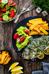 Grilled sea bream, French fries and fresh vegetables on wooden table