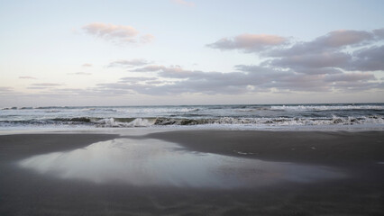 Panorama view of the ocean waves and beach under a sunset sky. The landscape reflection in the water. 